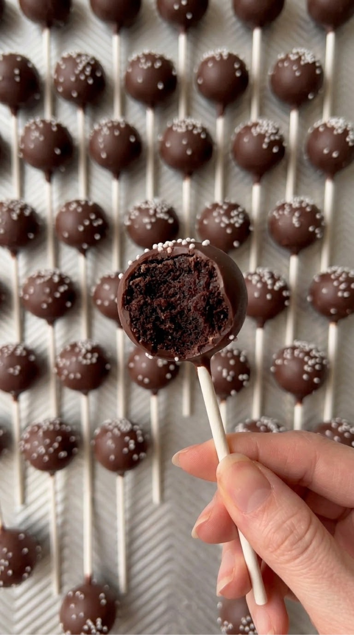 Chocolate cake pops with chocolate coating and pearl sprinkles, including one cut open