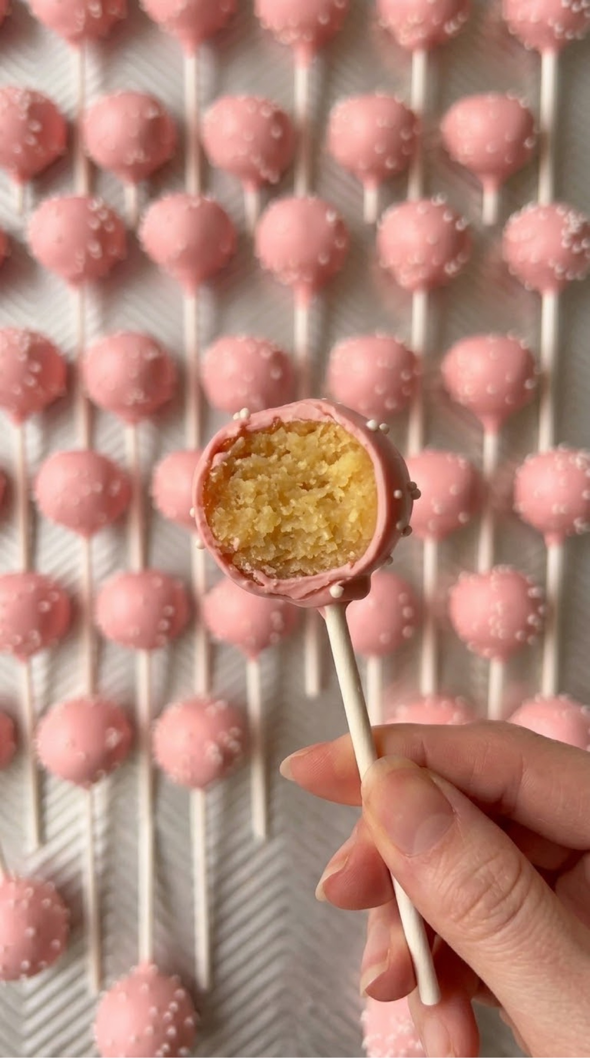Strawberry vanilla cake pops with pink coating and white pearl sprinkles, including one cut open